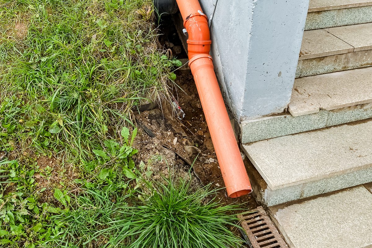 Discharge pipe running down beside basement steps to a channel drain